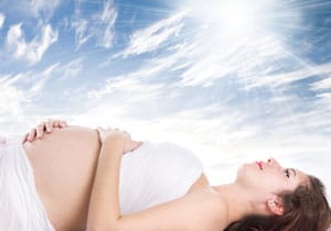 Schwangere liegt unter einem blauen Himmel und badet in der Sonne