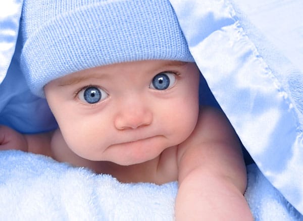 Baby mit blauen Augen schaut unter einer Decke hervor.