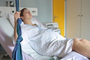Frau liegt im Klinikbett in den Wehen und hält sich an einem Seil fest. Im Hintergrund läuft ein CTG